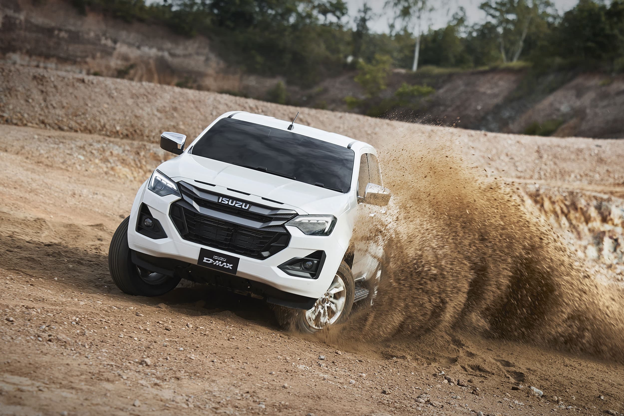 White ISUZU D-MAX truck drifting on a dirt road, kicking up dust, with a rugged landscape in the background.
